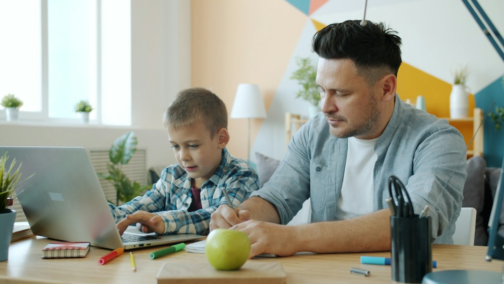A father guiding his son as they use a laptop together at home